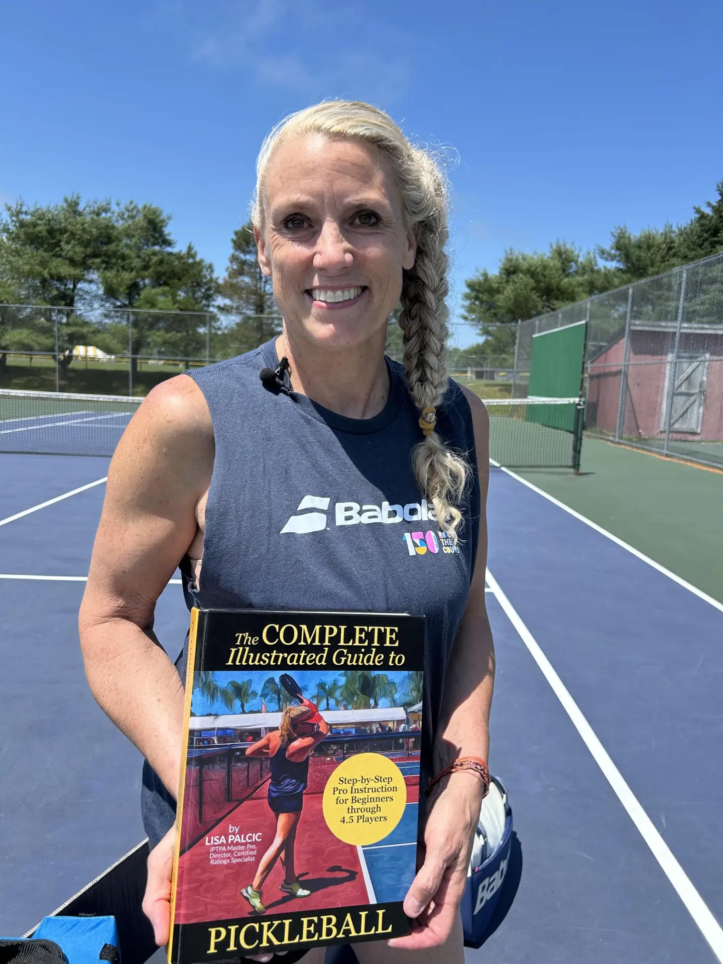 Lisa Palcic, IPTPA Master Pickleball Pro, holding her book on a pickleball court